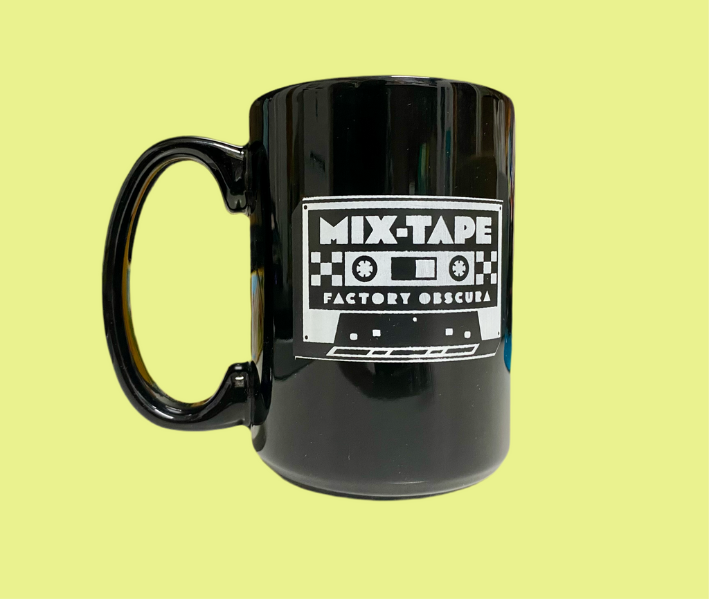 Black mug with white lettering saying MIXTAPE: Factory Obscura in the shape of a cassette tape. 